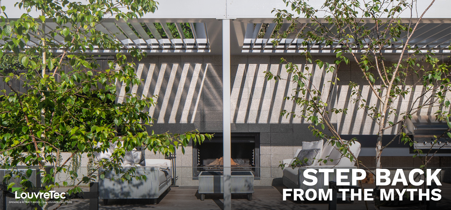 Opening roof with adjustable louvered blades creating striped shade over an outdoor lounge area with fireplace and trees