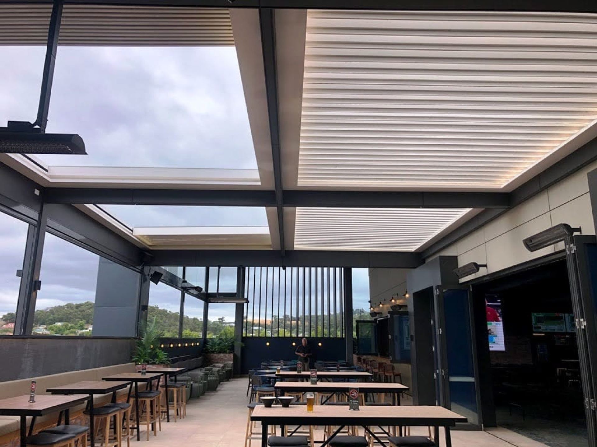 Outdoor dining area with a motorised retractable louvre roof, adjustable shade panels, and glass walls, showcasing the benefits of a retractable roof system.
