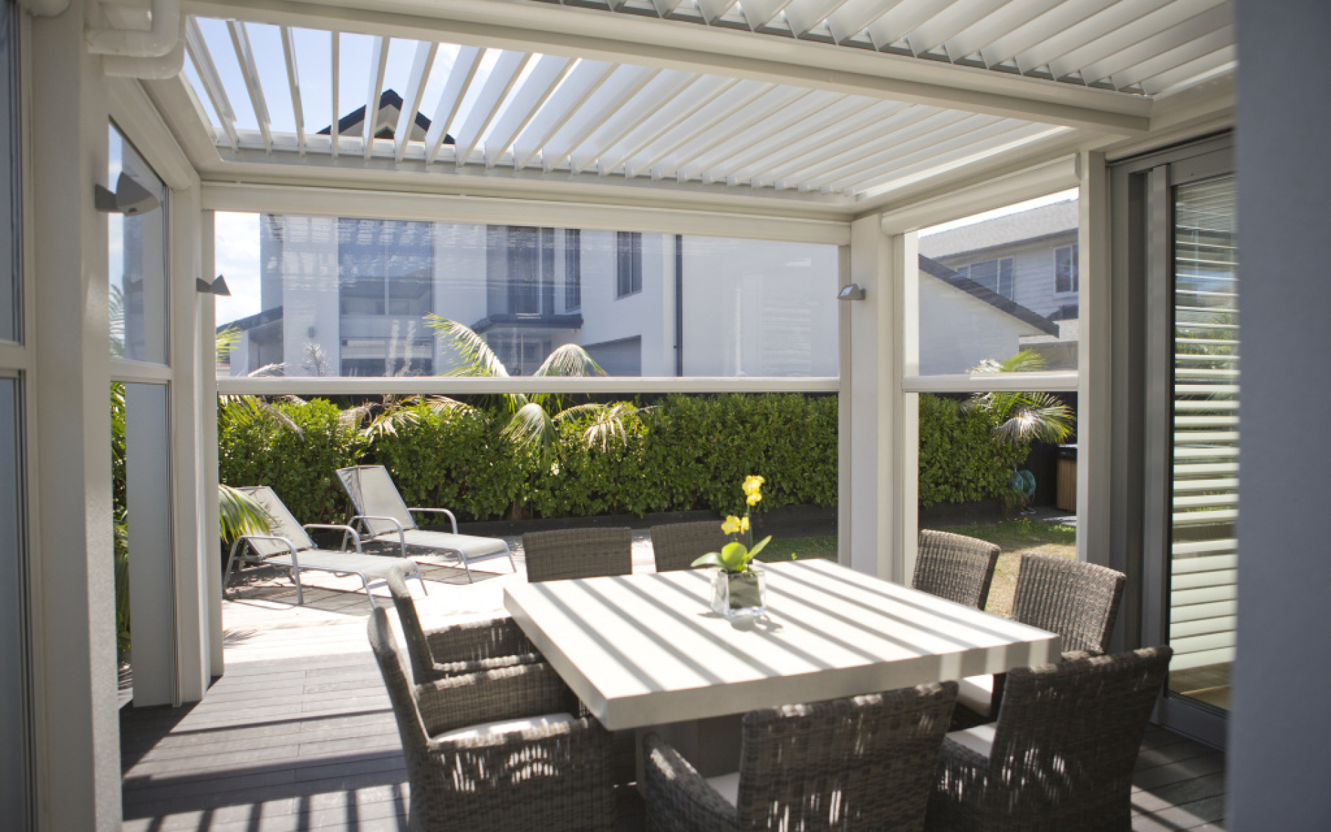 Modern patio area with outdoor blinds and louvre roof system, providing shade and privacy for a dining table and chairs in a stylish garden setting.
