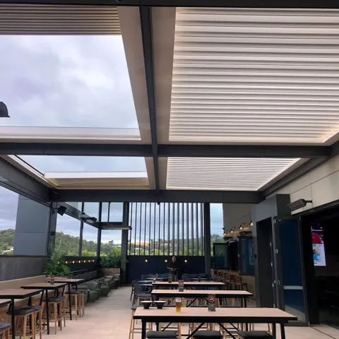 Outdoor dining area with a motorised retractable louvre roof, adjustable shade panels, and glass walls, showcasing the benefits of a retractable roof system.