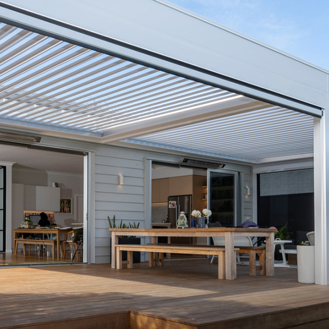 Opening roof system with adjustable louvered blades covering a timber deck and outdoor dining area attached to a modern home