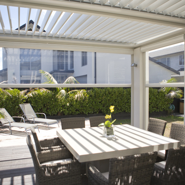 Modern patio area with outdoor blinds and louvre roof system, providing shade and privacy for a dining table and chairs in a stylish garden setting.