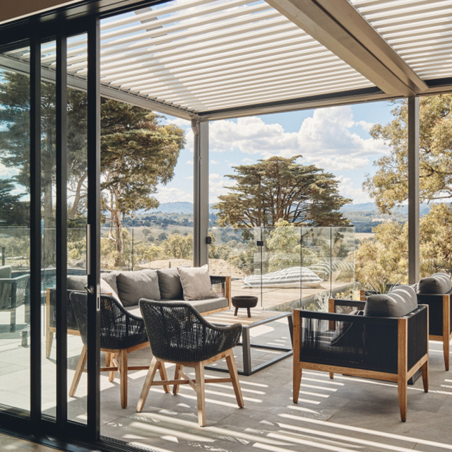 A luxurious patio with outdoor furniture under a louvered pergola, overlooking a scenic landscape.
